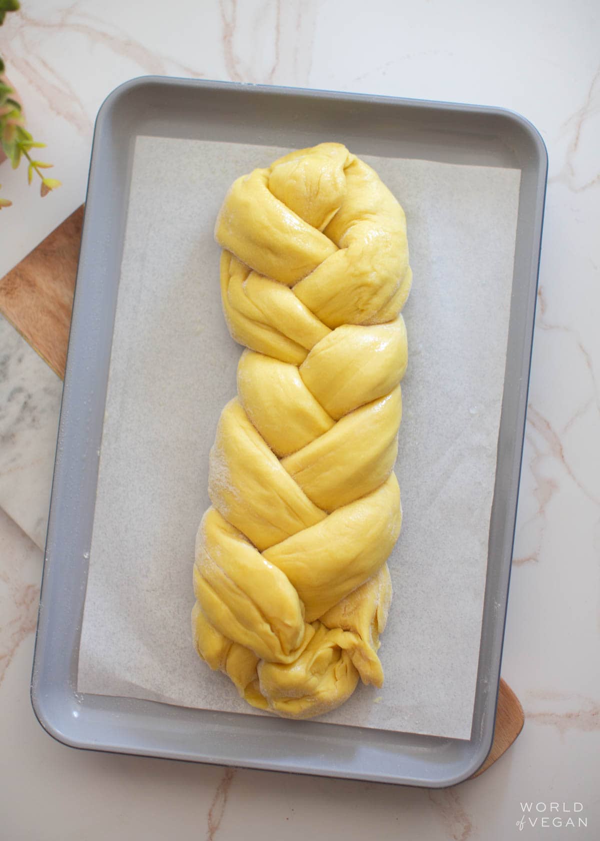 Three-strand braided vegan challah bread on a baking tray.