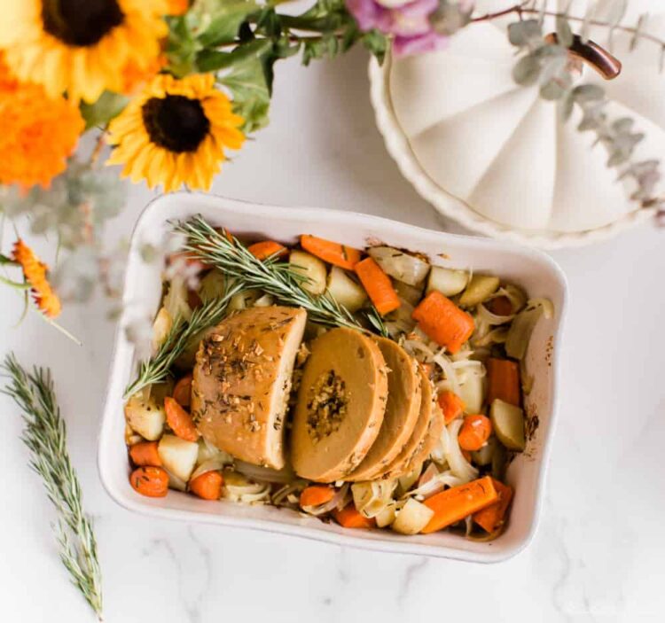 Tofurky roast sliced, in a baking dish on top of roasted vegetables.