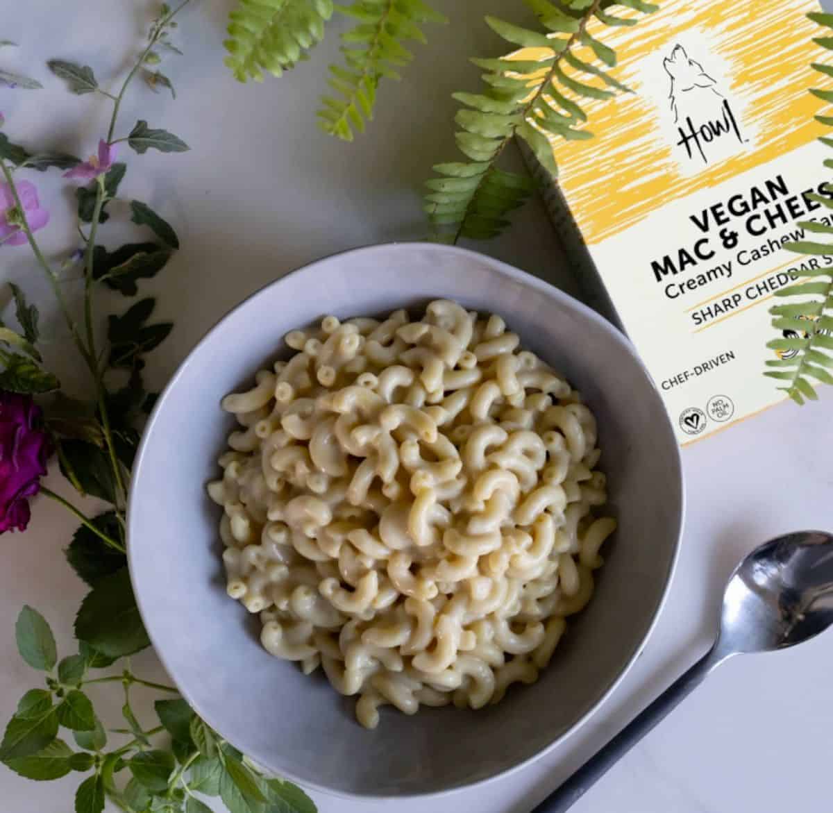 A creamy bowl of Howl's vegan mac and cheese next to a spoon and the box of packaging.