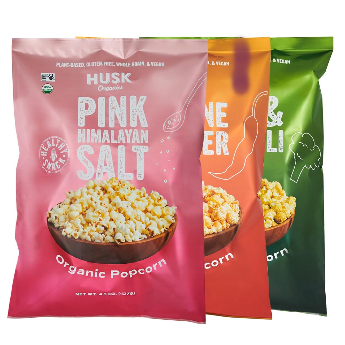 A pink, orange and green bag of Husk Organics popcorn against a white background. 