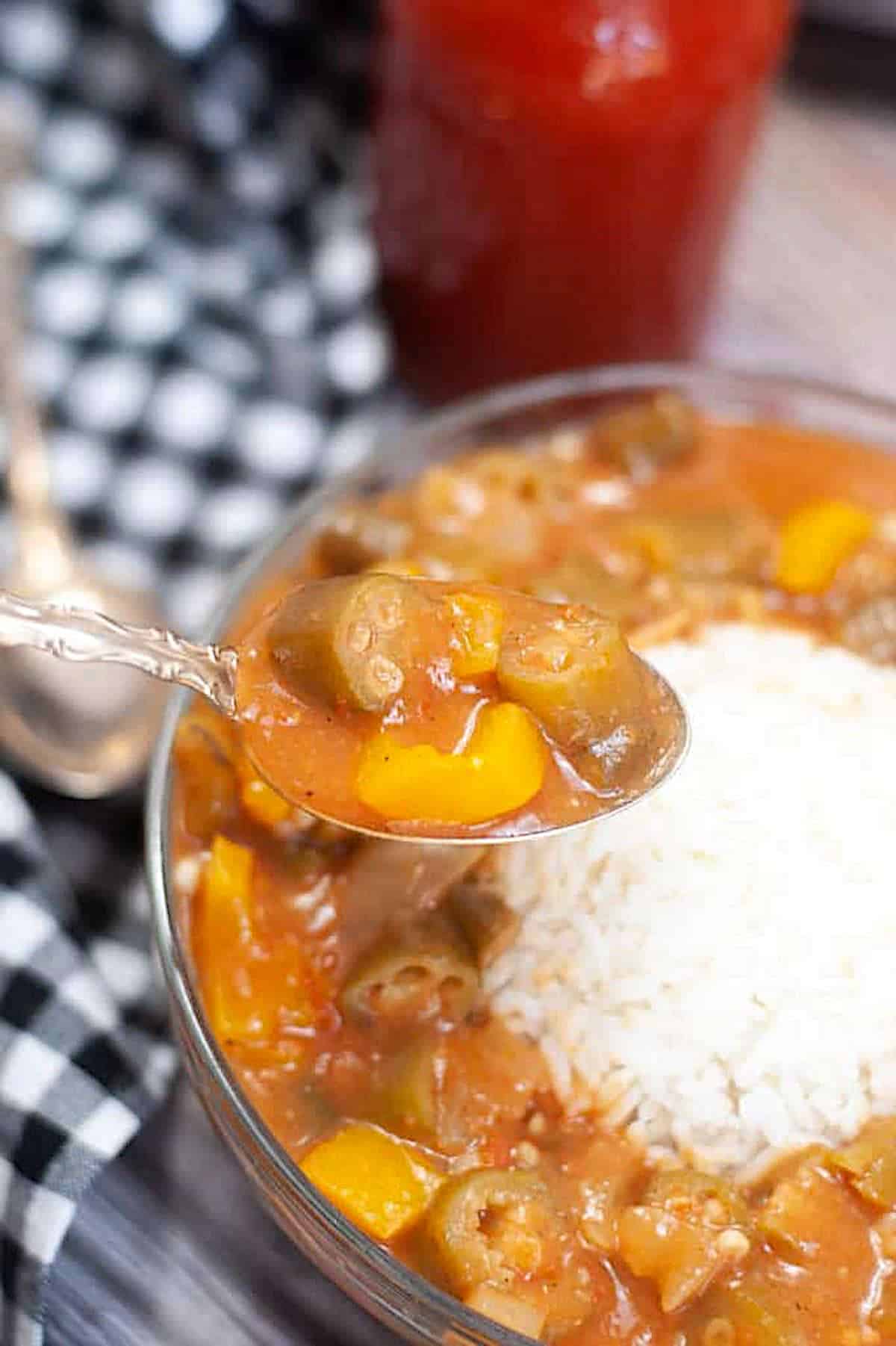 A spoon holding a bite of vegan gumbo over a bowl filled with gumbo and rice.