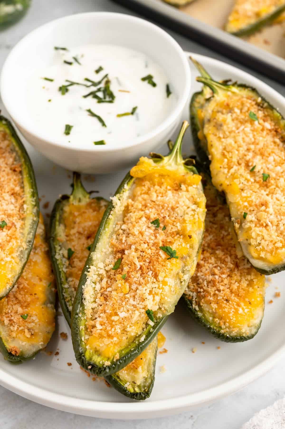 A close-up shot of jalapeno poppers on a white plate with a small bowl of white dip.