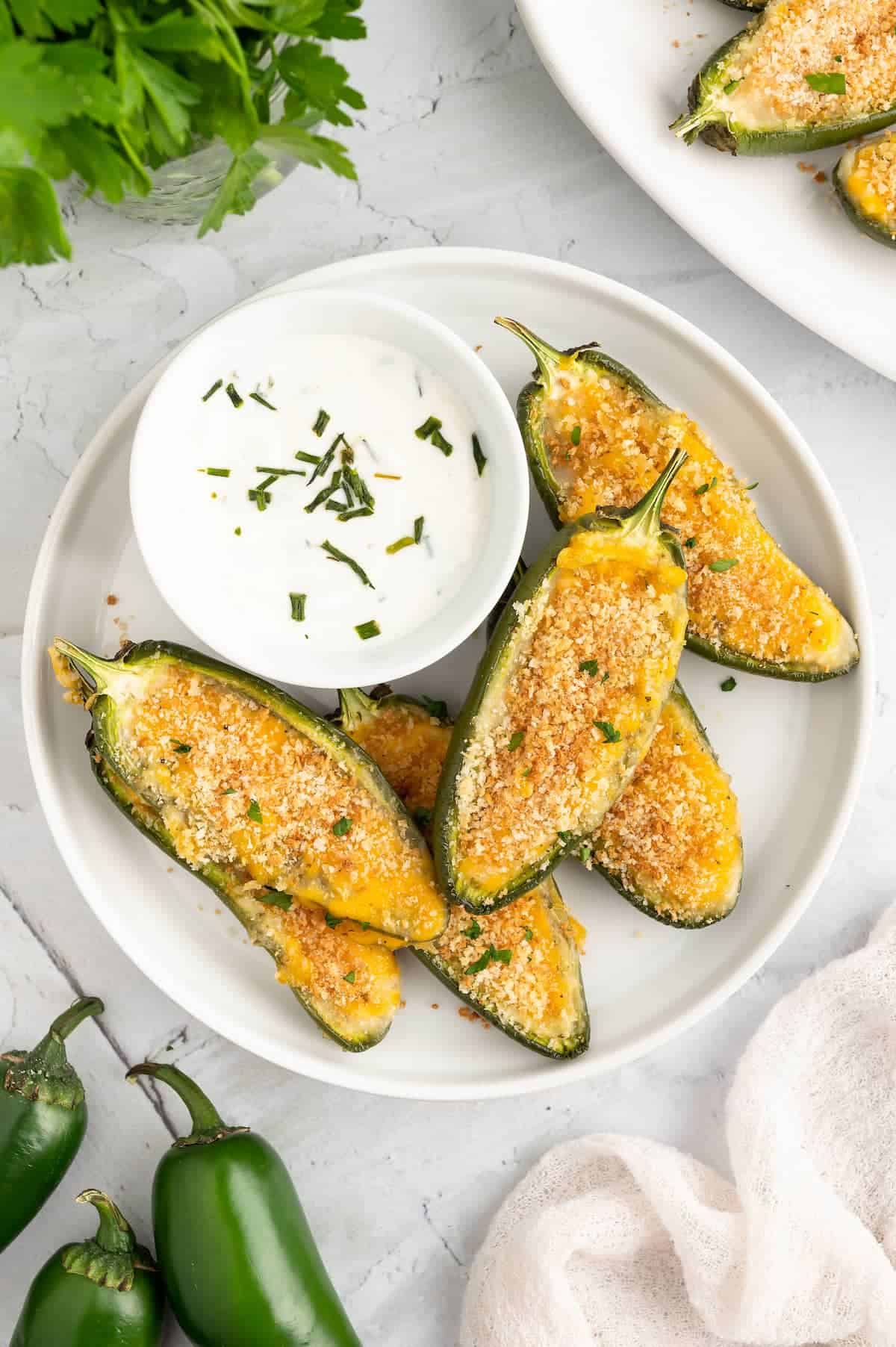 Jalapeno poppers on a white plate with dip against a marble background.