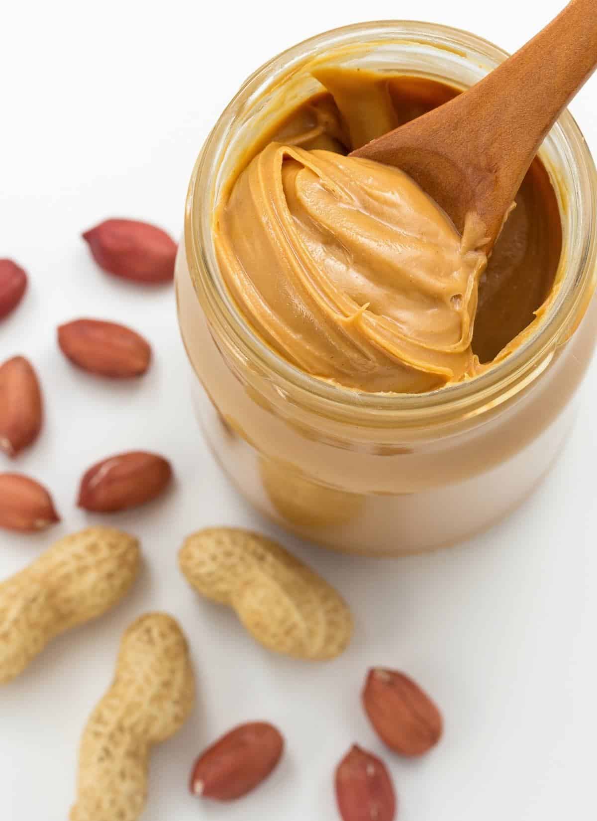Wooden spoon scooping homemade peanut butter out of a jar. 