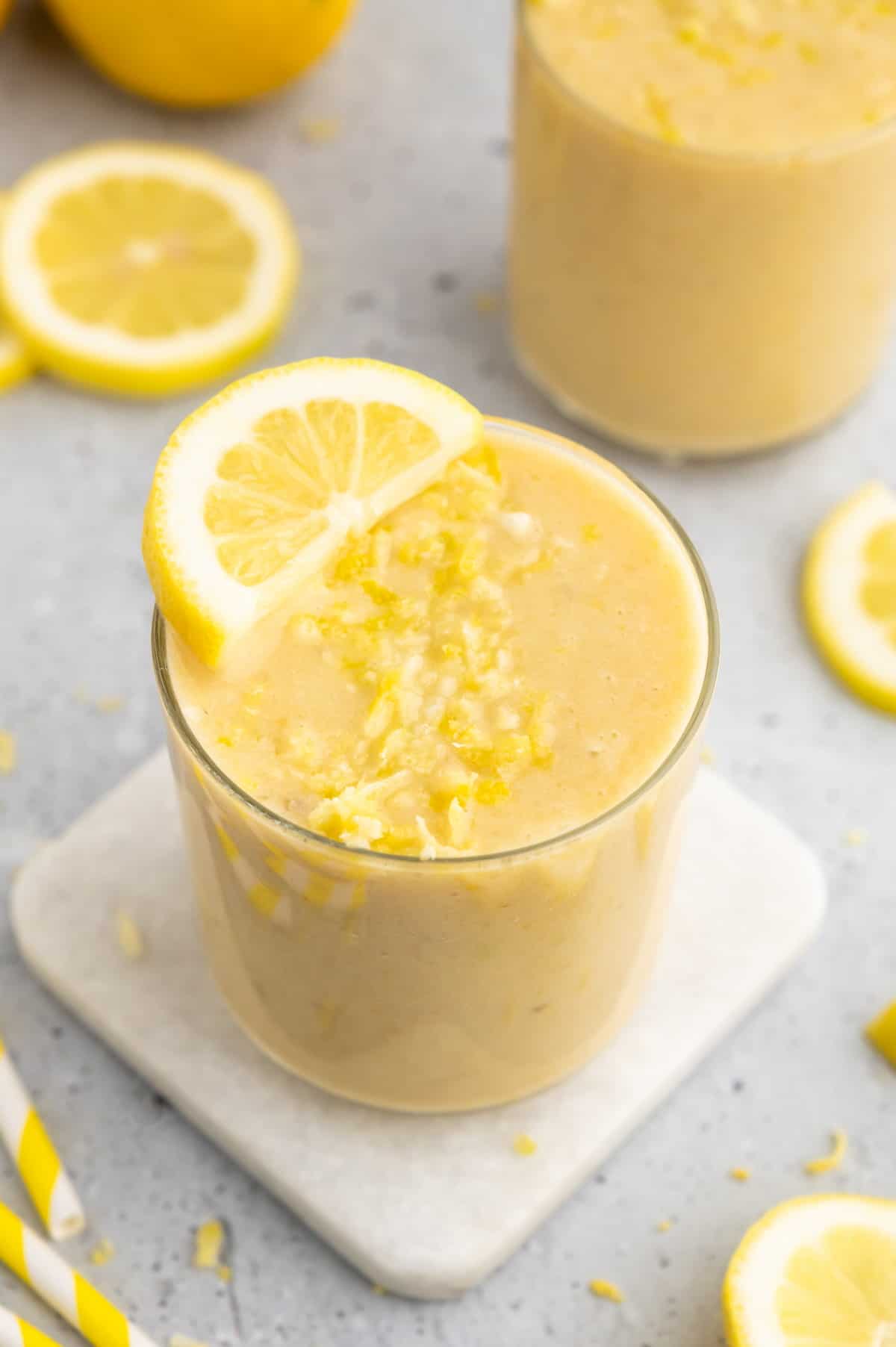 Lemon smoothie in a glass topped with a lemon slice and zest.