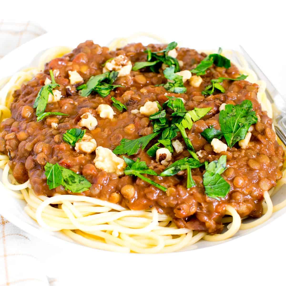 A plate of lentil bolognese served over spaghetti and topped with fresh herbs.