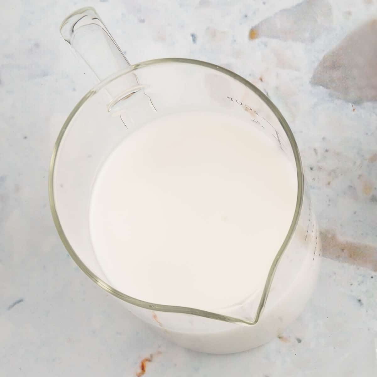 A glass measuring cup for fluid ounces and cups filled with non-dairy milk.
