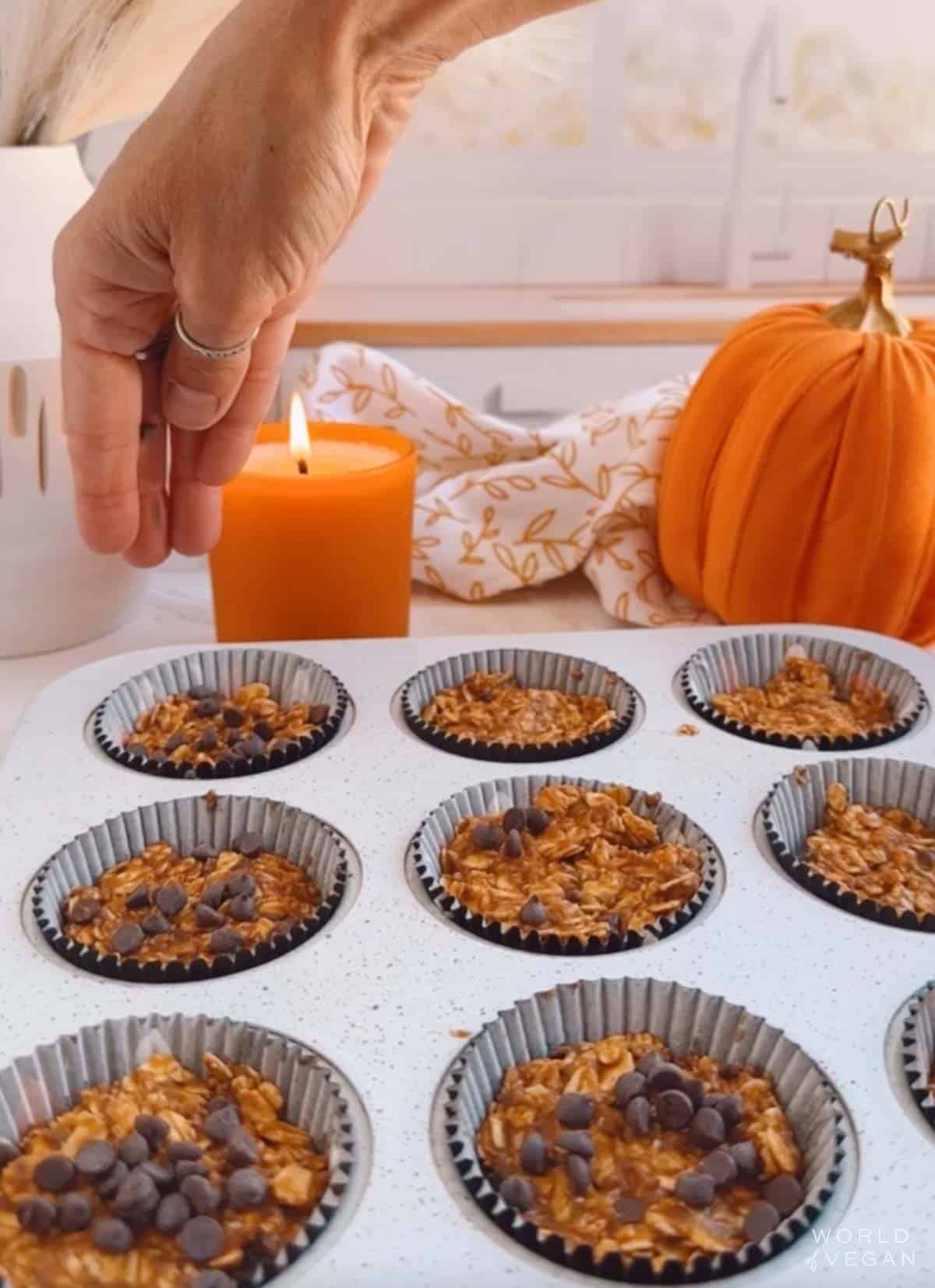 The oatmeal bites batter added to a muffin pan, with a hand sprinkling additional chocolate chips over top.