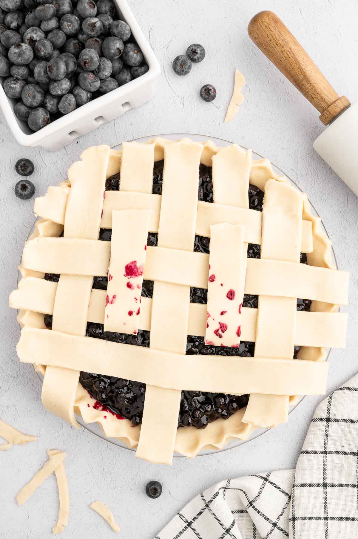 A partial lattice pattern with the pie crust dough strips on top of the blueberry pie.