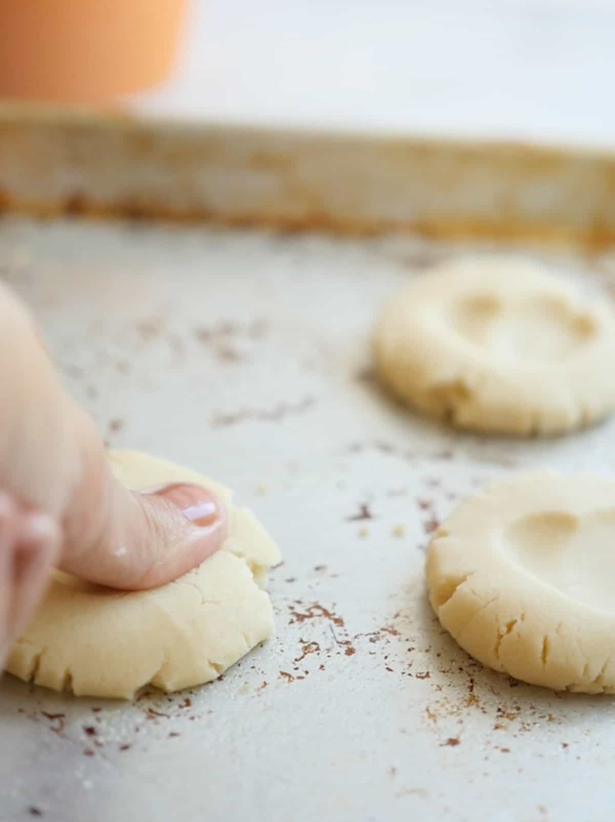 Thumb pressing into flattened cookies on a baking tray to form a heart shape.