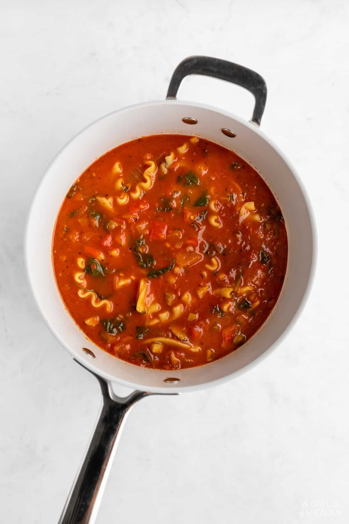 Cooking the lasagna soup marinara broth in a saucepan with veggies and herbs.