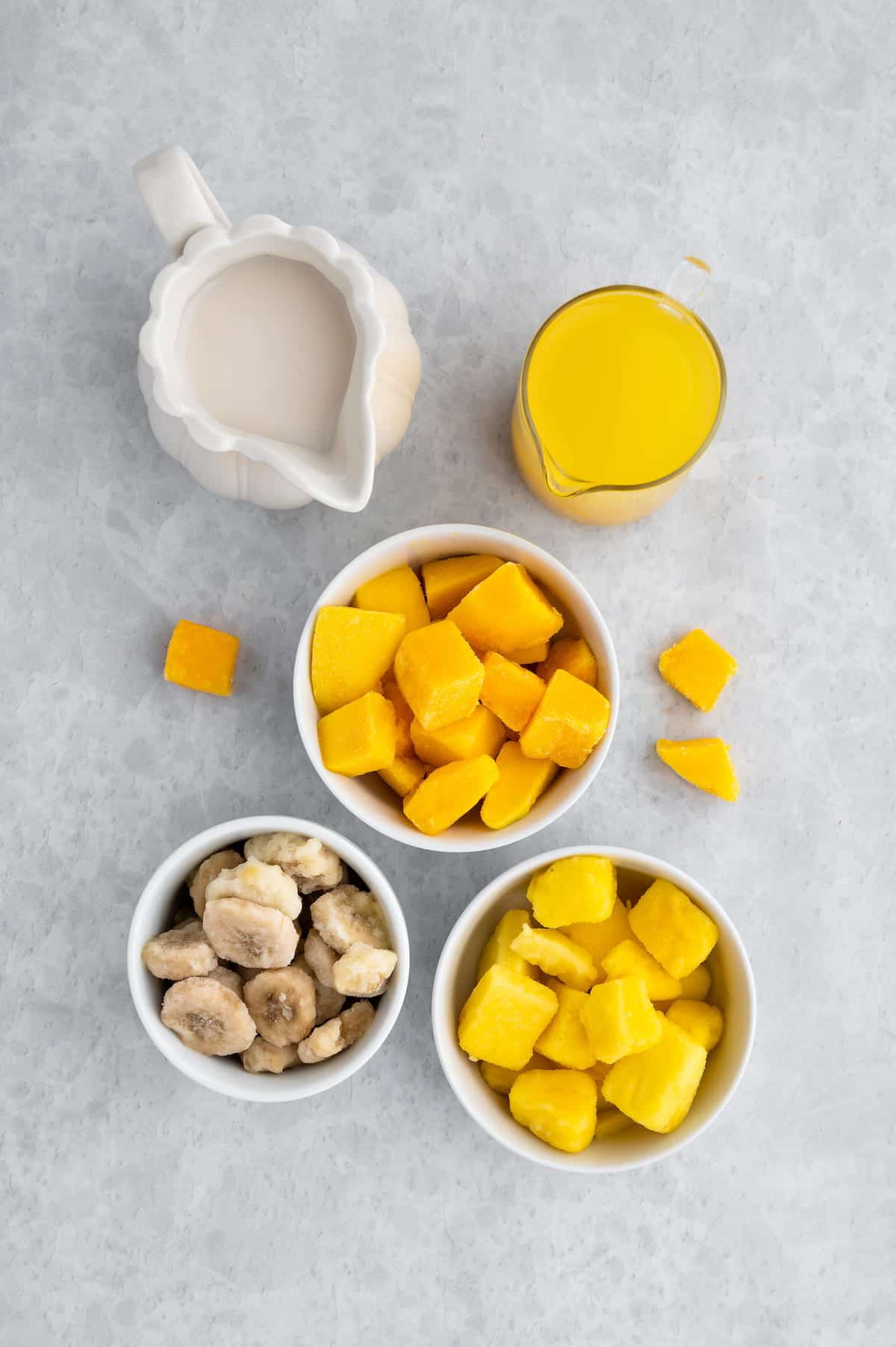 Overhead view of ingredients for mango pineapple smoothie including frozen banana and plant-based milk.
