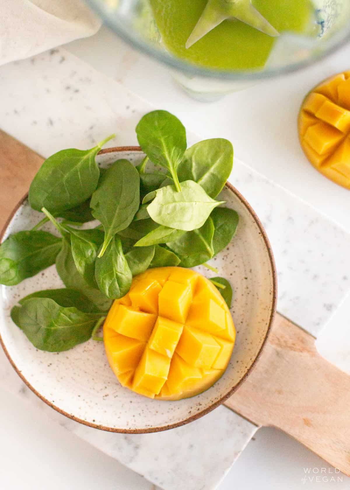 A cut mango and spinach leaves on a plate.