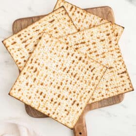 Matzah crackers in a stack on top of a wooden pizza tray.