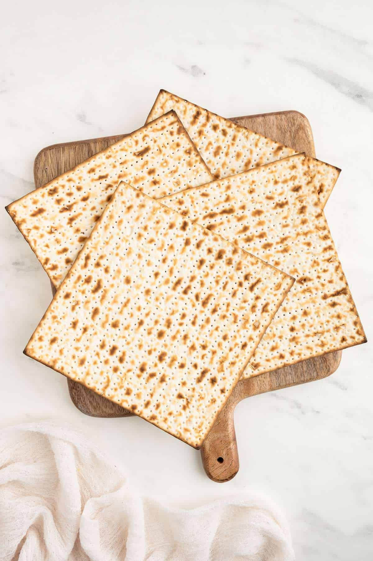 Matzah crackers in a stack on top of a wooden pizza tray.