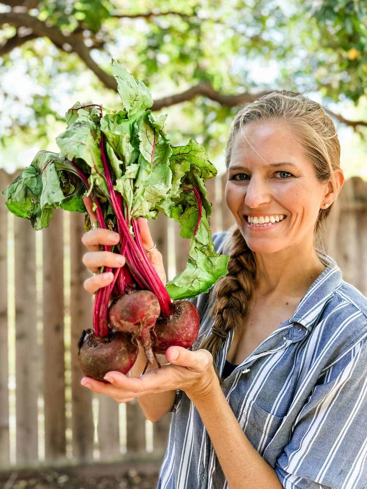 A woman holding out a bundle of fresh raw red beets with their greens.