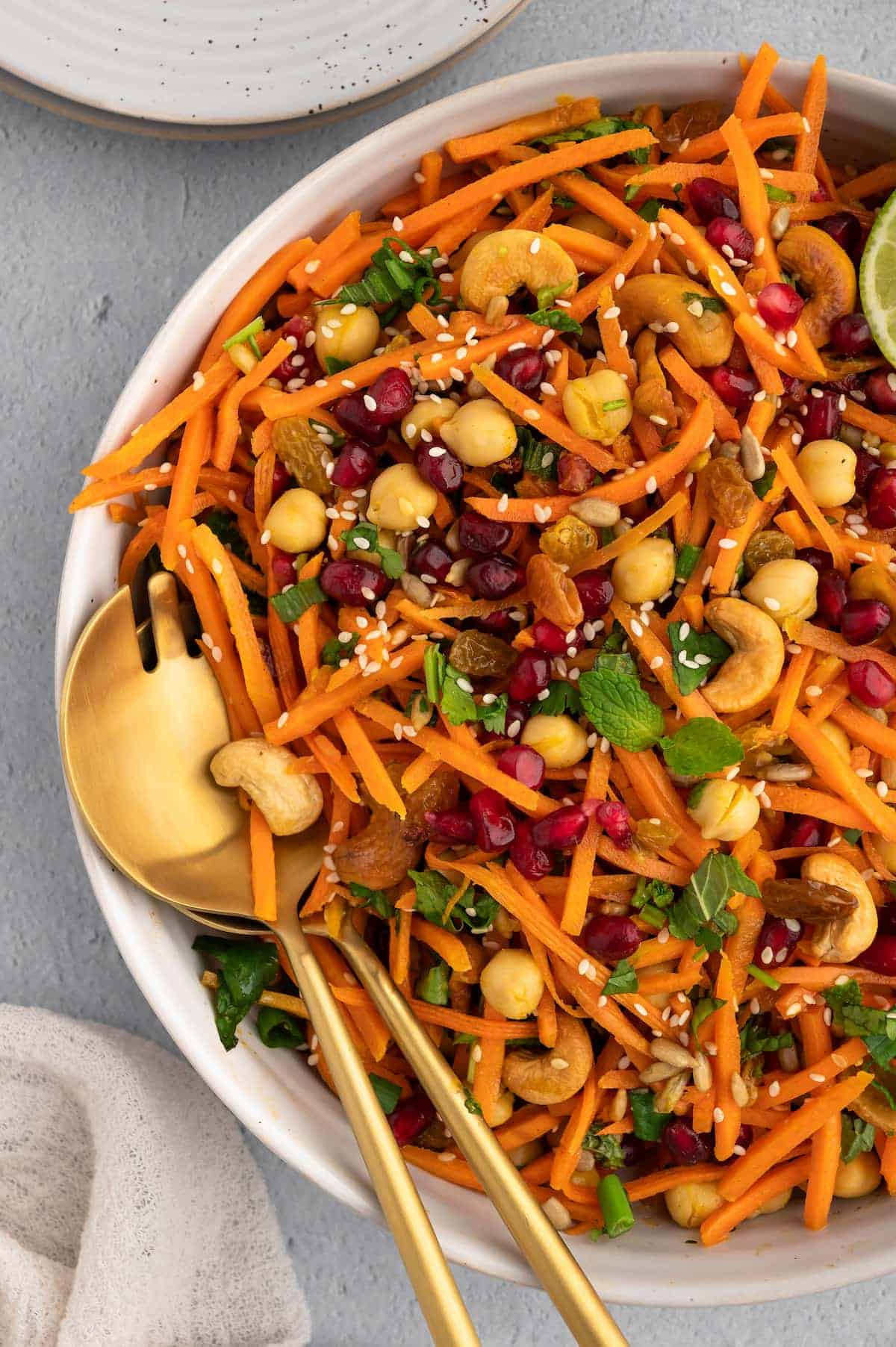 A large bowl of Moroccan carrot salad with gold serving utensils.