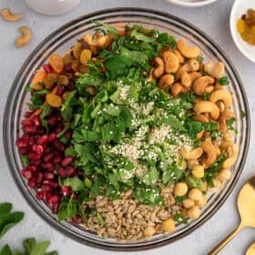 A bowl of greens, cashews, pomegranate seeds and sunflower seeds.