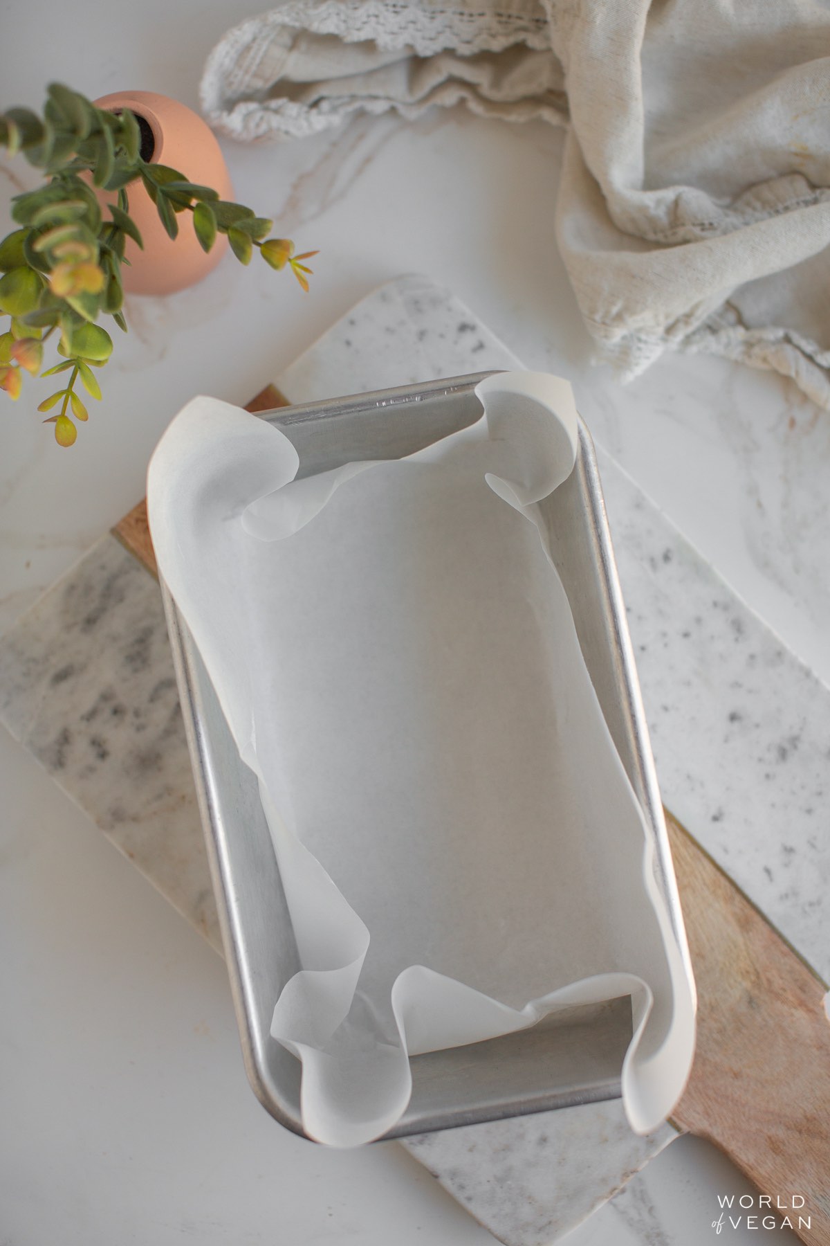 Metal loaf pan lined with parchment paper on a cutting board. 