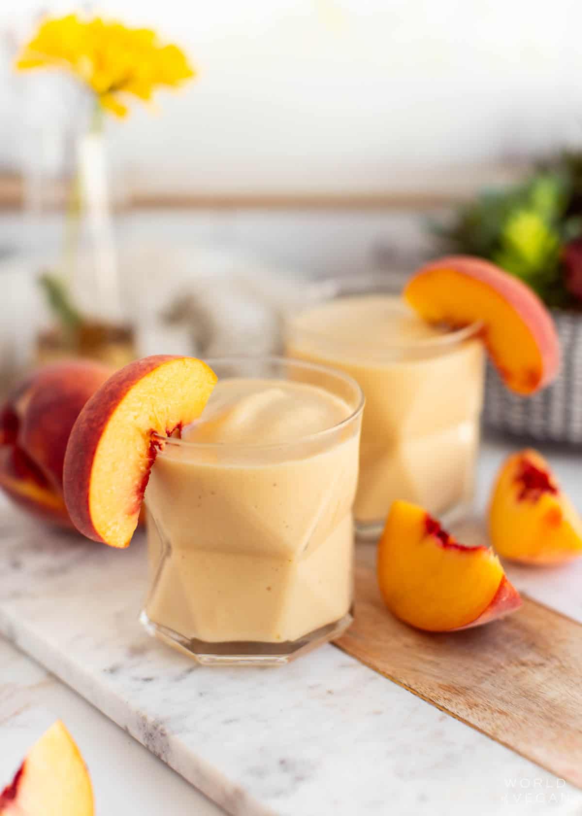 Two banana peach smoothies in glasses with peach slices.
