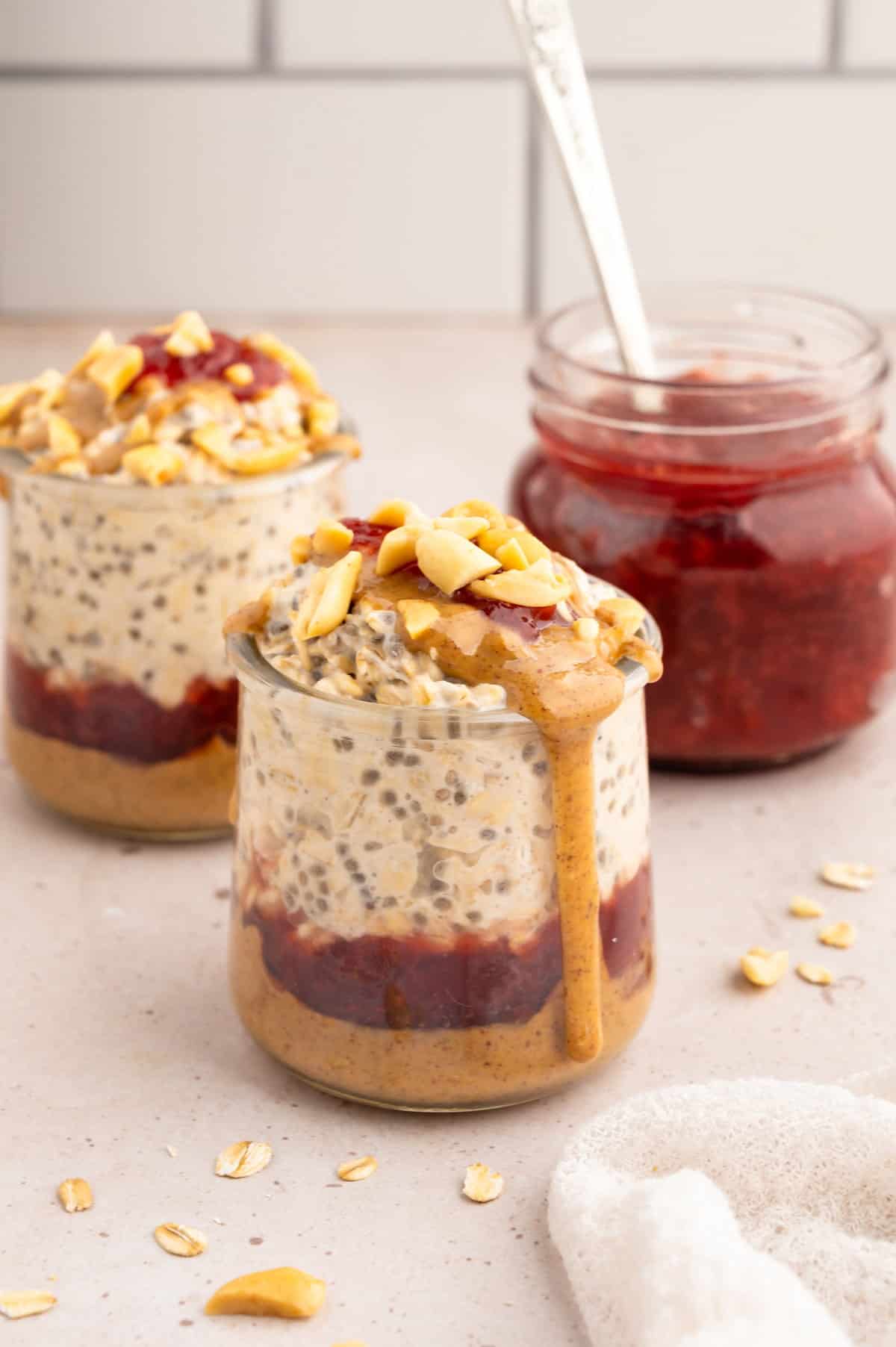 Two jars of peanut butter overnight oats with jelly in the background.