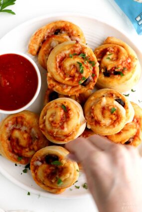 Woman sprinkling chopped parsley on the pizza rolls.