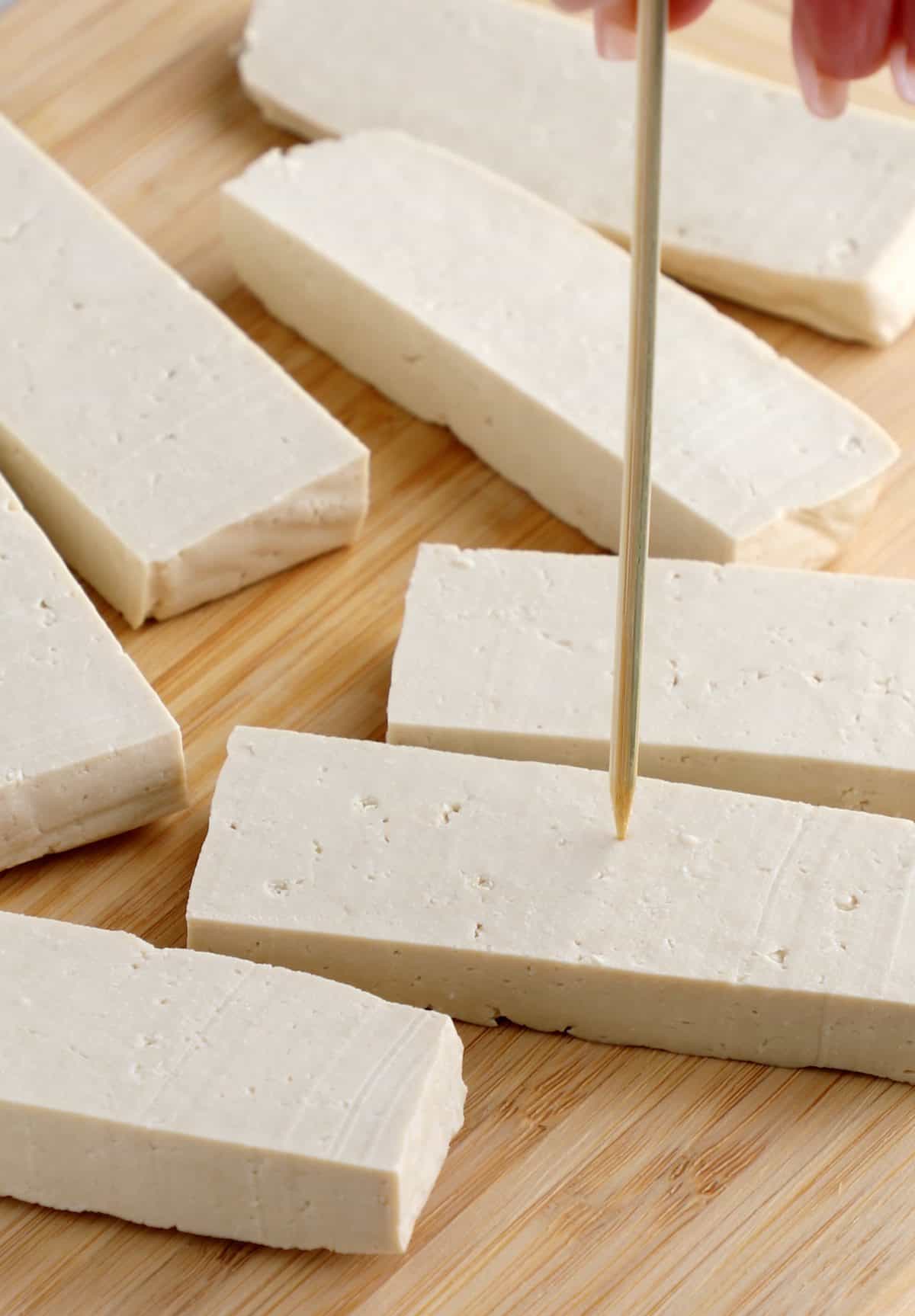 Sliced tofu being pierced with a skewer.