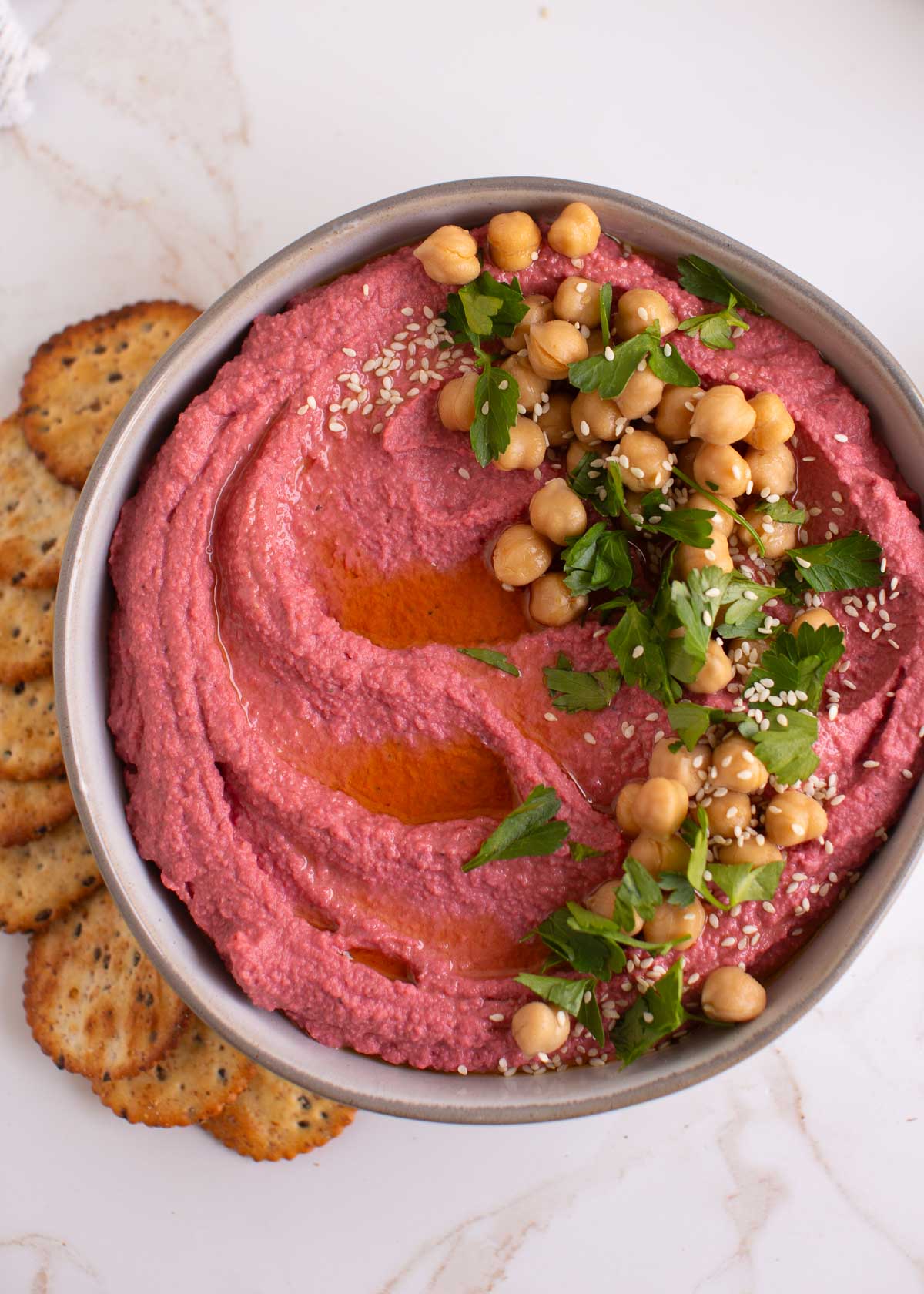 Serving pink hummus with olive oil drizzle, sesame seeds, and toppings. 