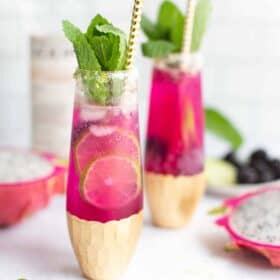 Pink cocktail in an elegant glass with mint garnish and a gold striped paper straw.