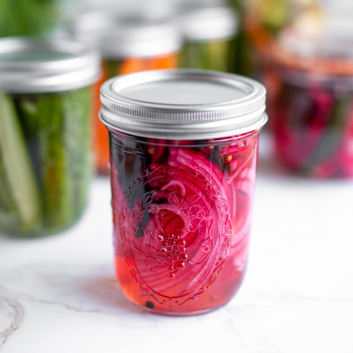 Pink pickled red onion in a glass jar with a lid.