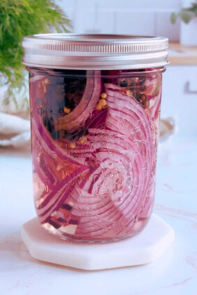 Pink pickled red onions sealed in a glass jar.