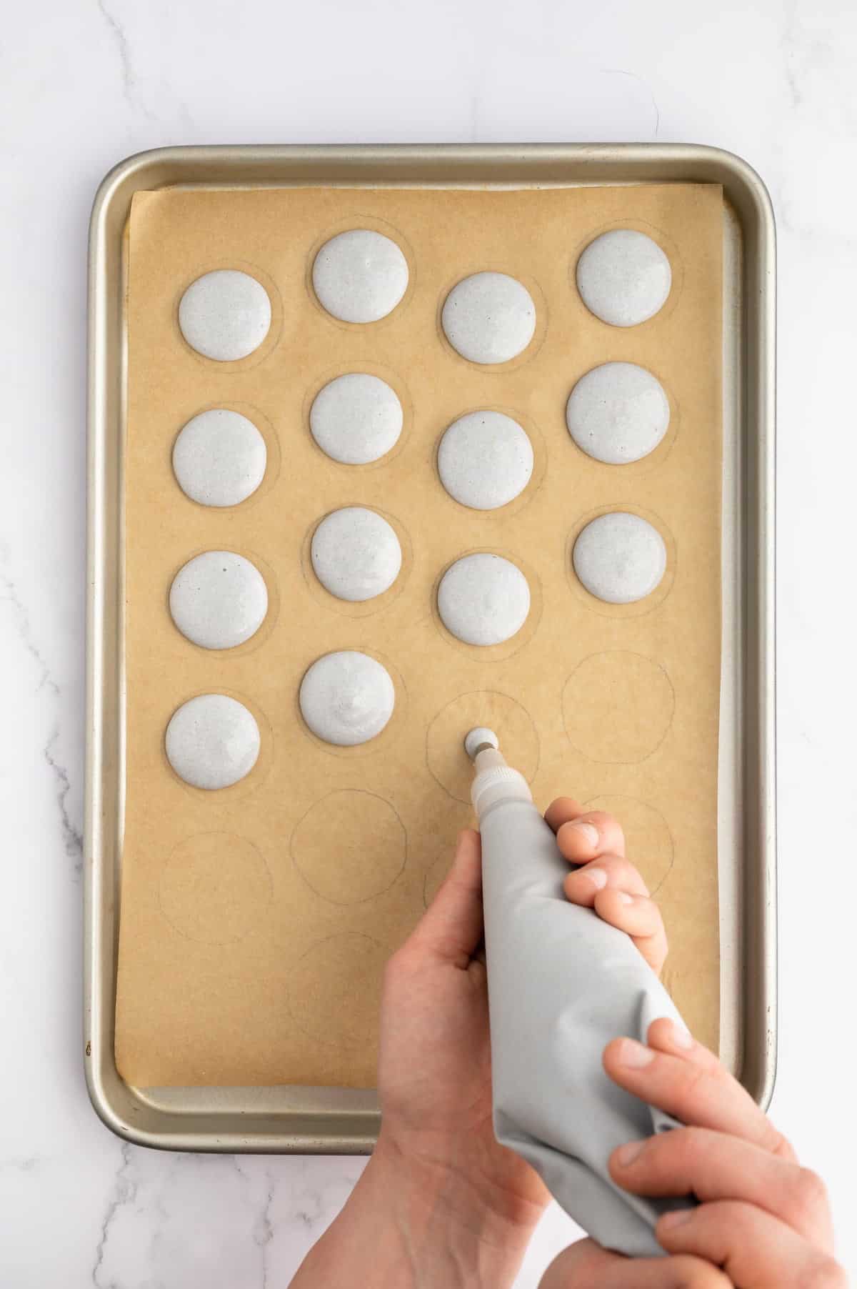 Piping vegan macaron batter onto a prepared baking sheet.