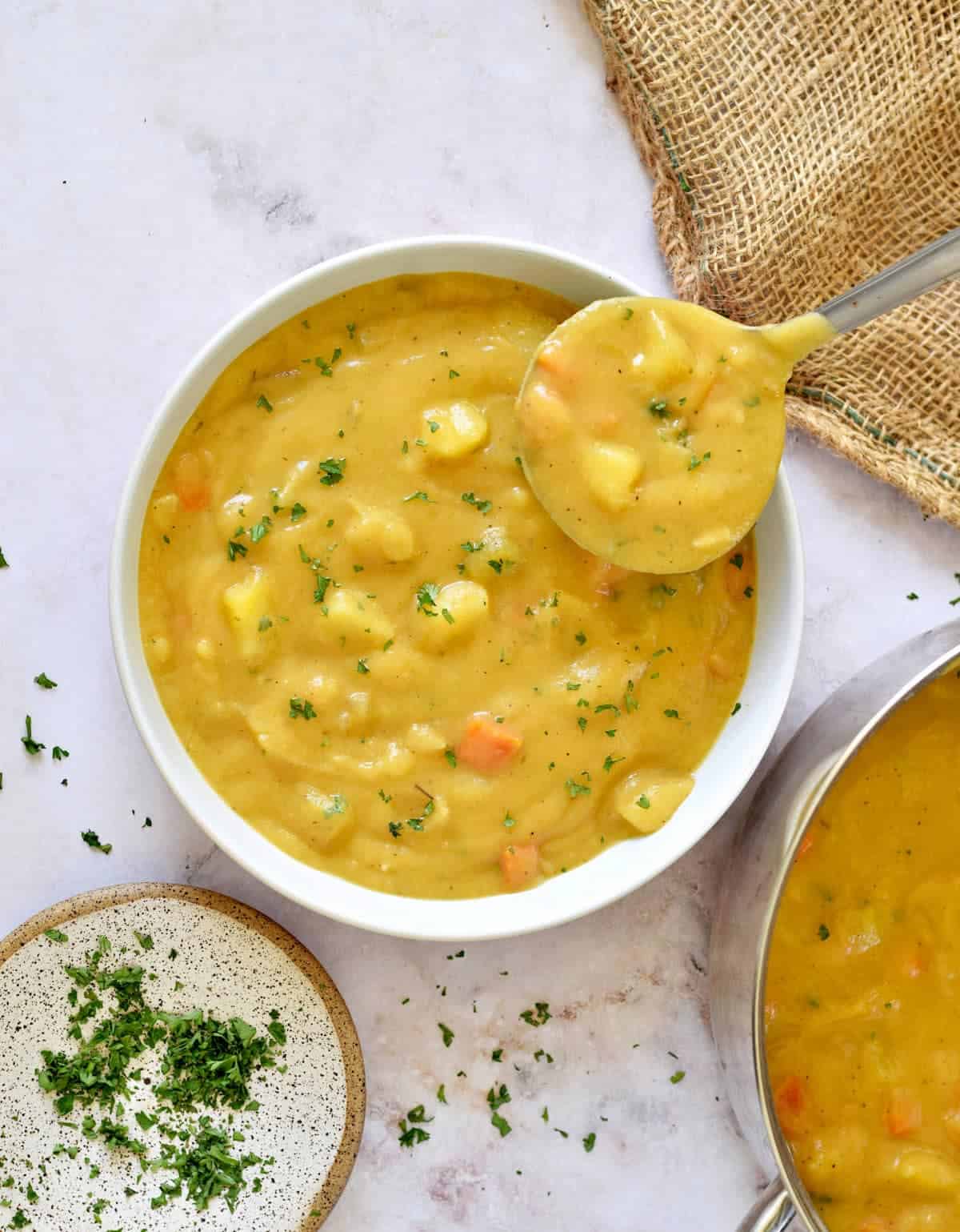 Large bowl of potato soup with a ladle next to a pot of soup.