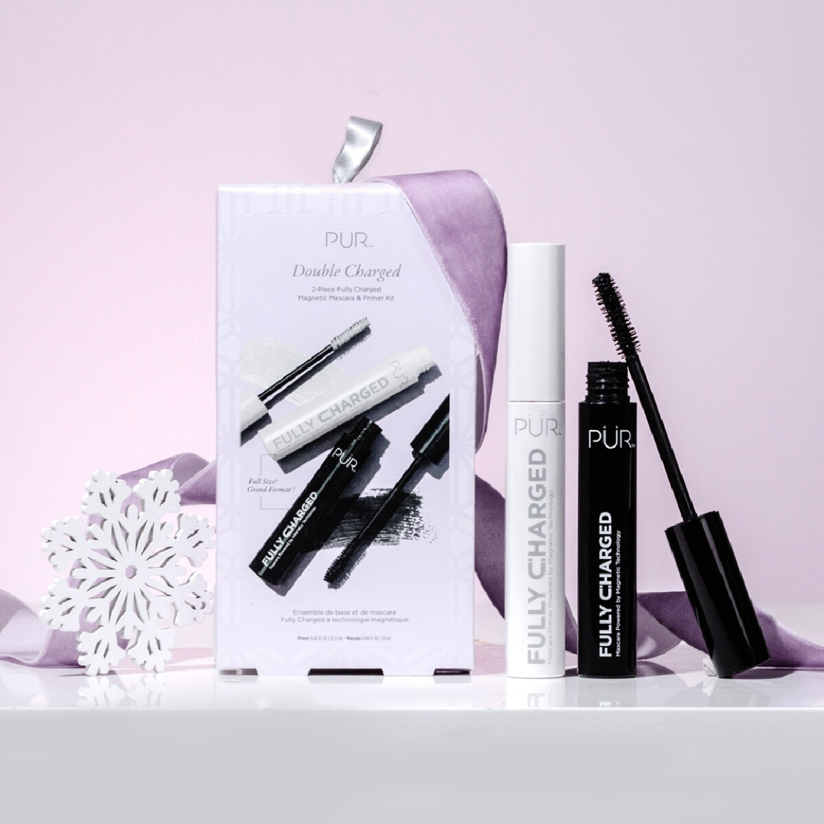 Pur Gift Set of Mascaras next to a white and black tube of Fully Charged Mascara against a light purple background with white snowflake.