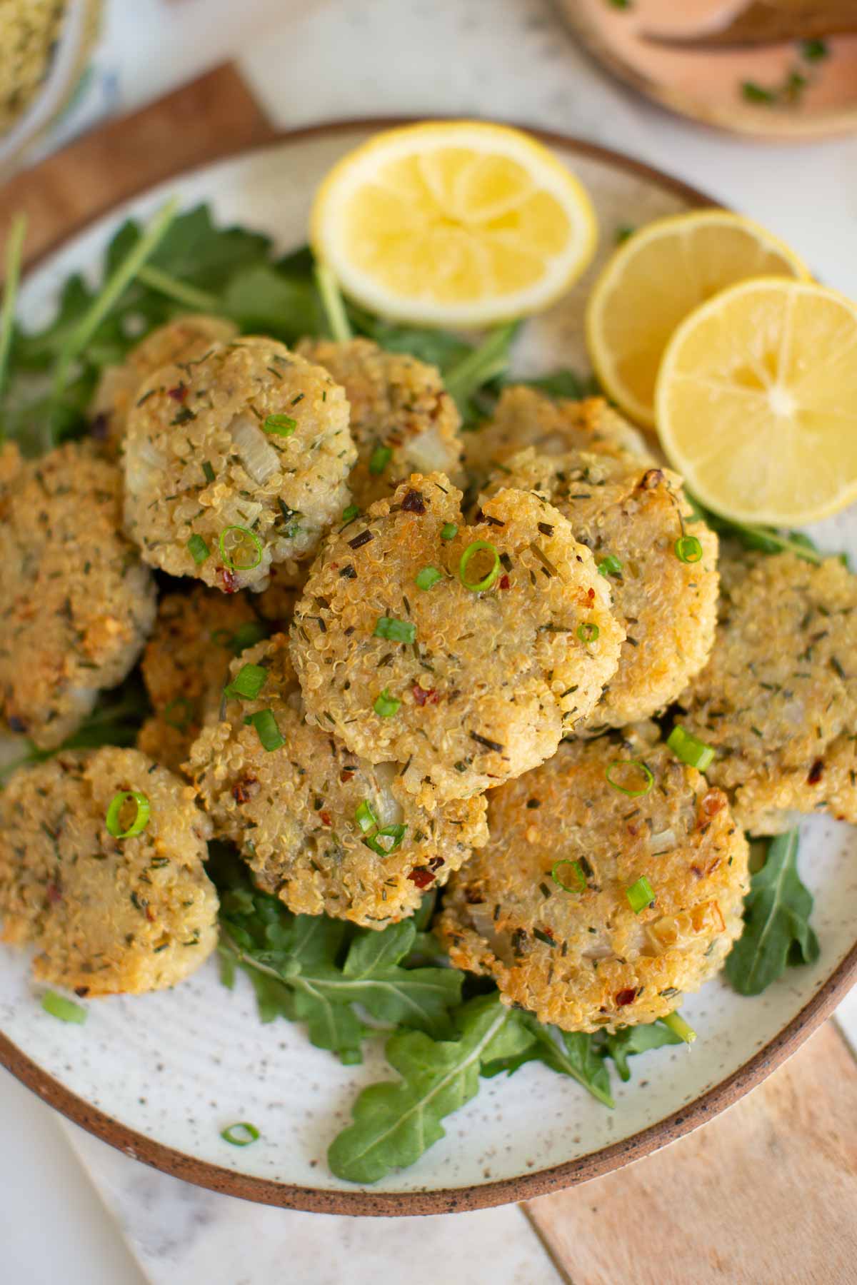 A plate of quinoa nugget bites served over a bed of arugula and served with sliced lemons.