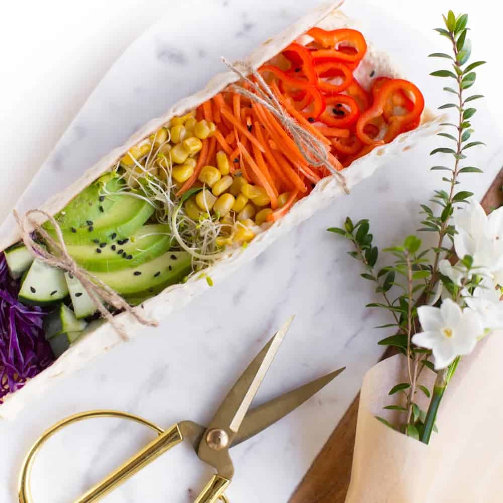 lavash wrap full of corn, avocado, cabbage, cucumber, shredded carrots, and red peppers on a 