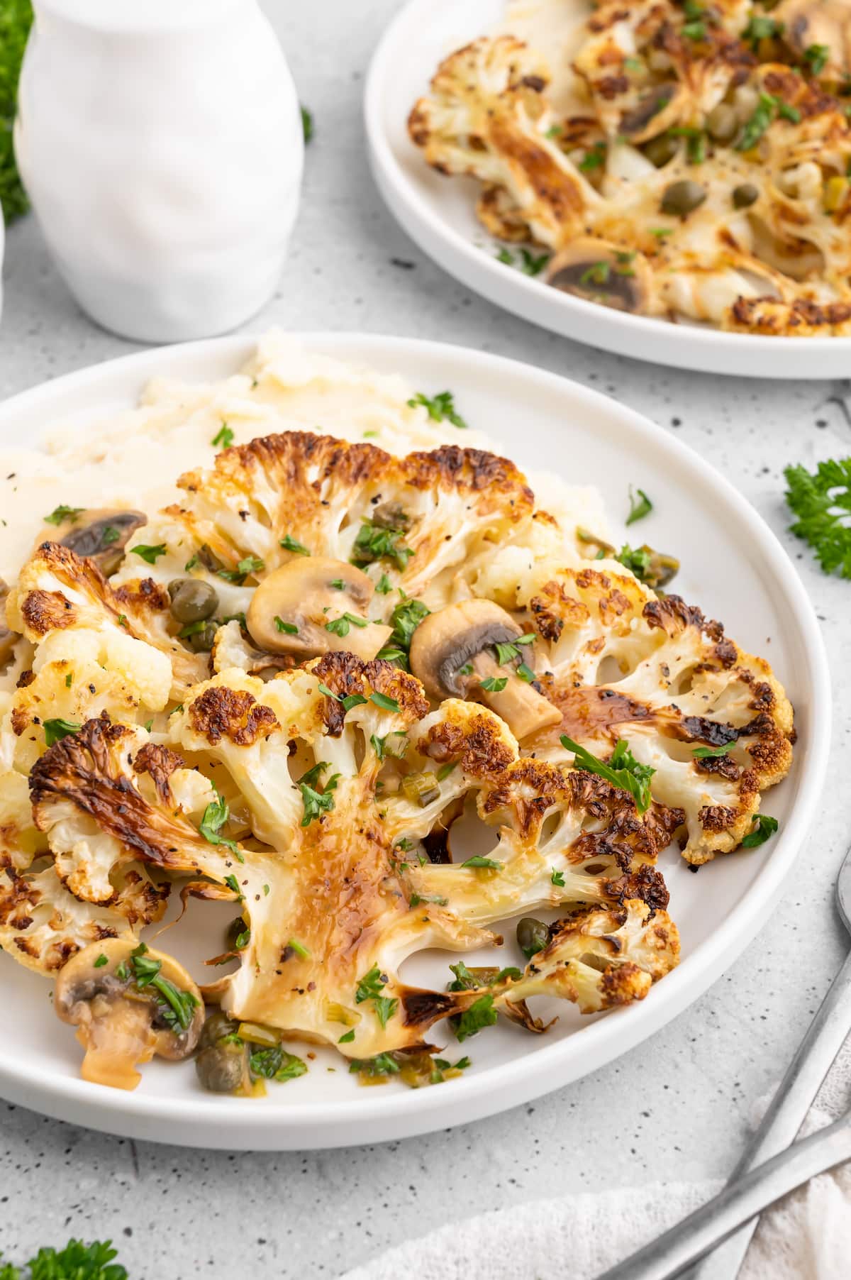 Cauliflower steaks on a plate of mashed potatoes, with piccata sauce on top.