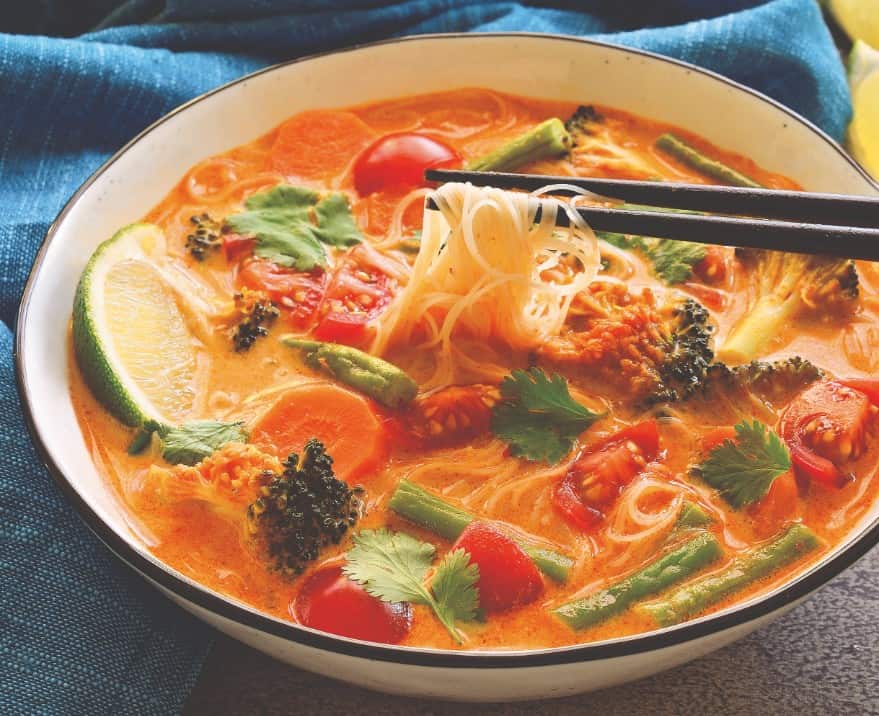 Vegan curry noodle soup in bowl with chop sticks.