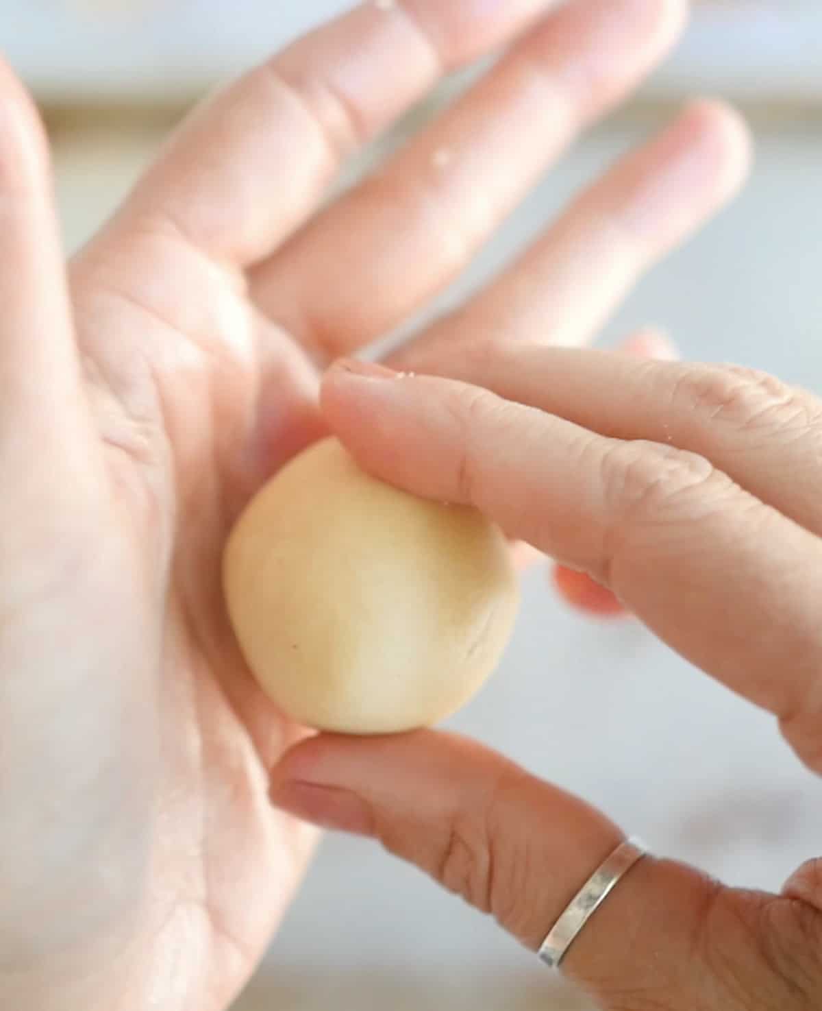 Hand rolling thumbprint cookie dough into a ball.