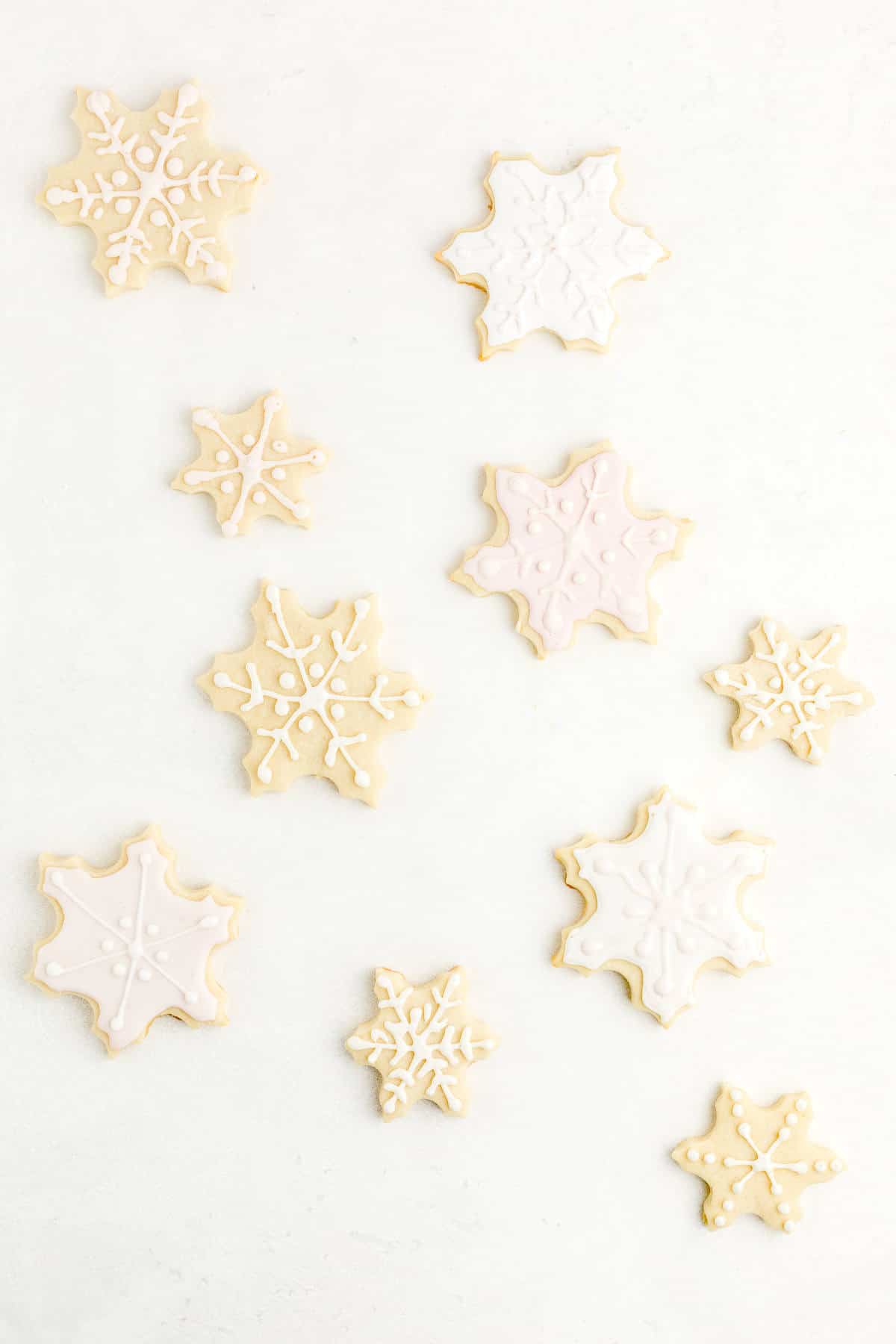 Snowflake-shaped sugar cookies on light background decorated with egg-free royal icing.