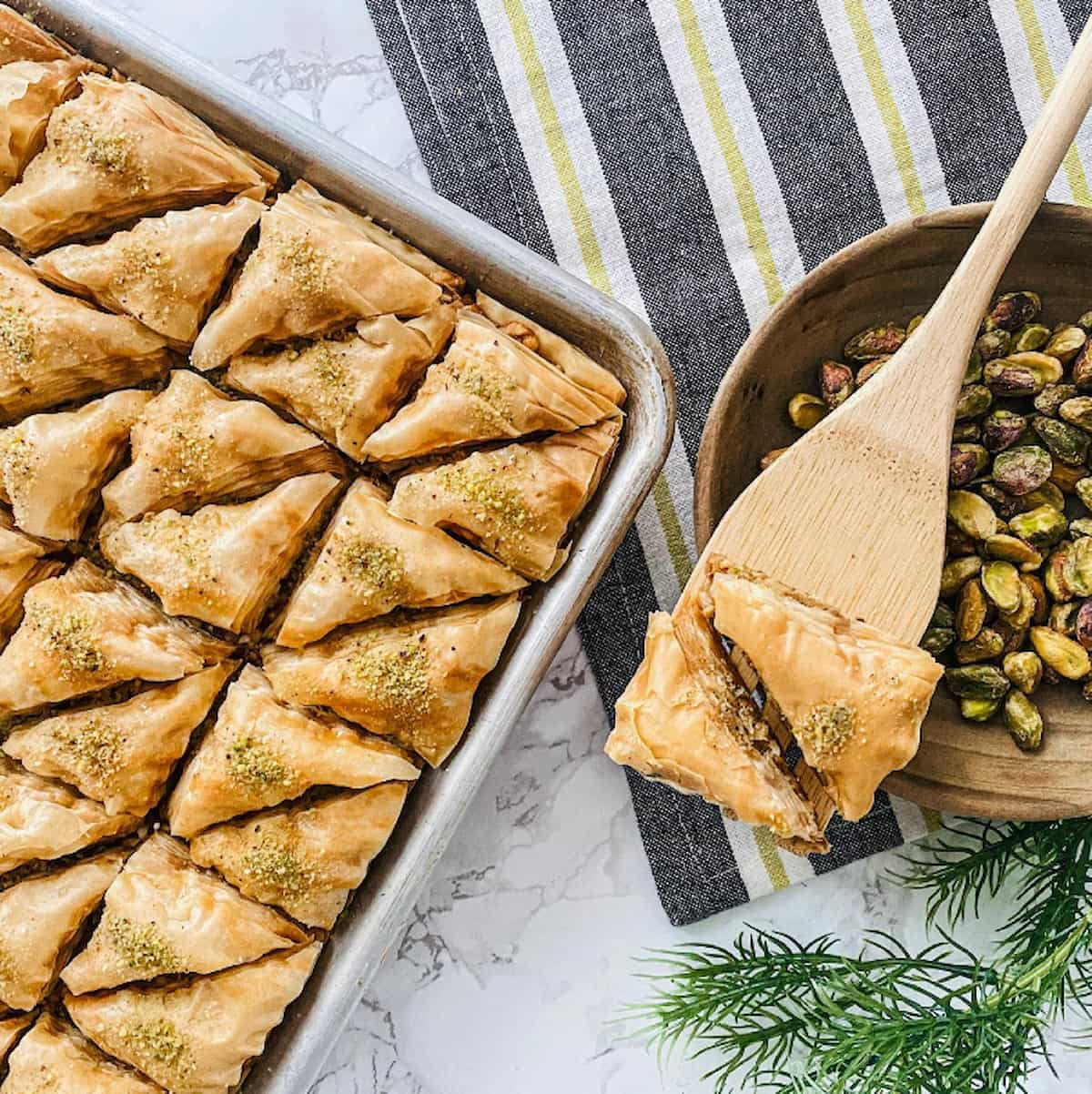 Vegan baklava in a pan with a wooden spatula holding a couple pieces.