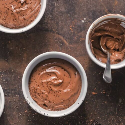 vegan chocolate pudding in multiple mugs against a brown surface