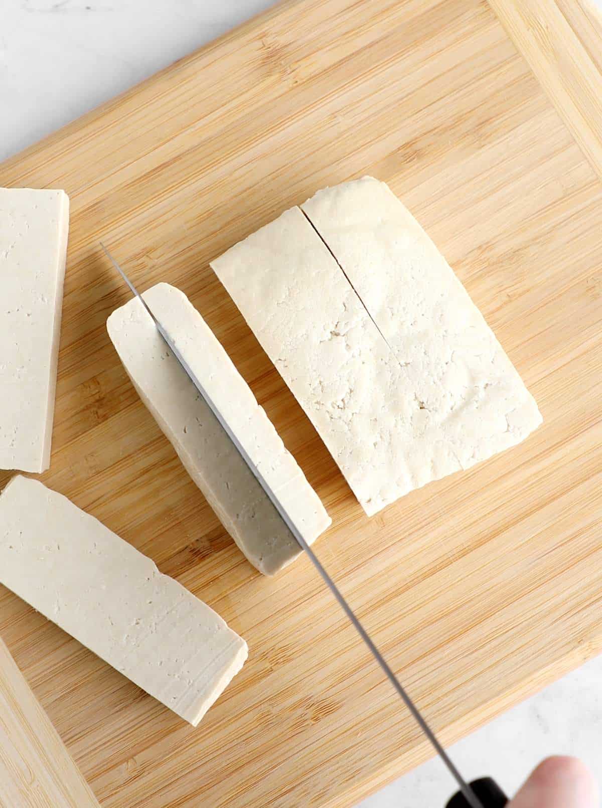 Tofu being sliced with a knife into strips.