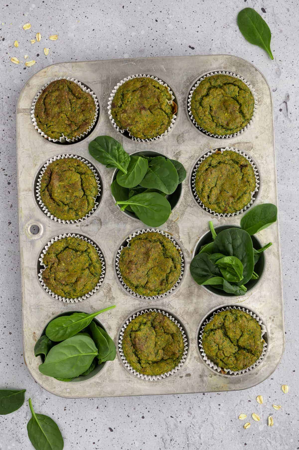 Spinach banana muffins in a muffin tin with spinach.