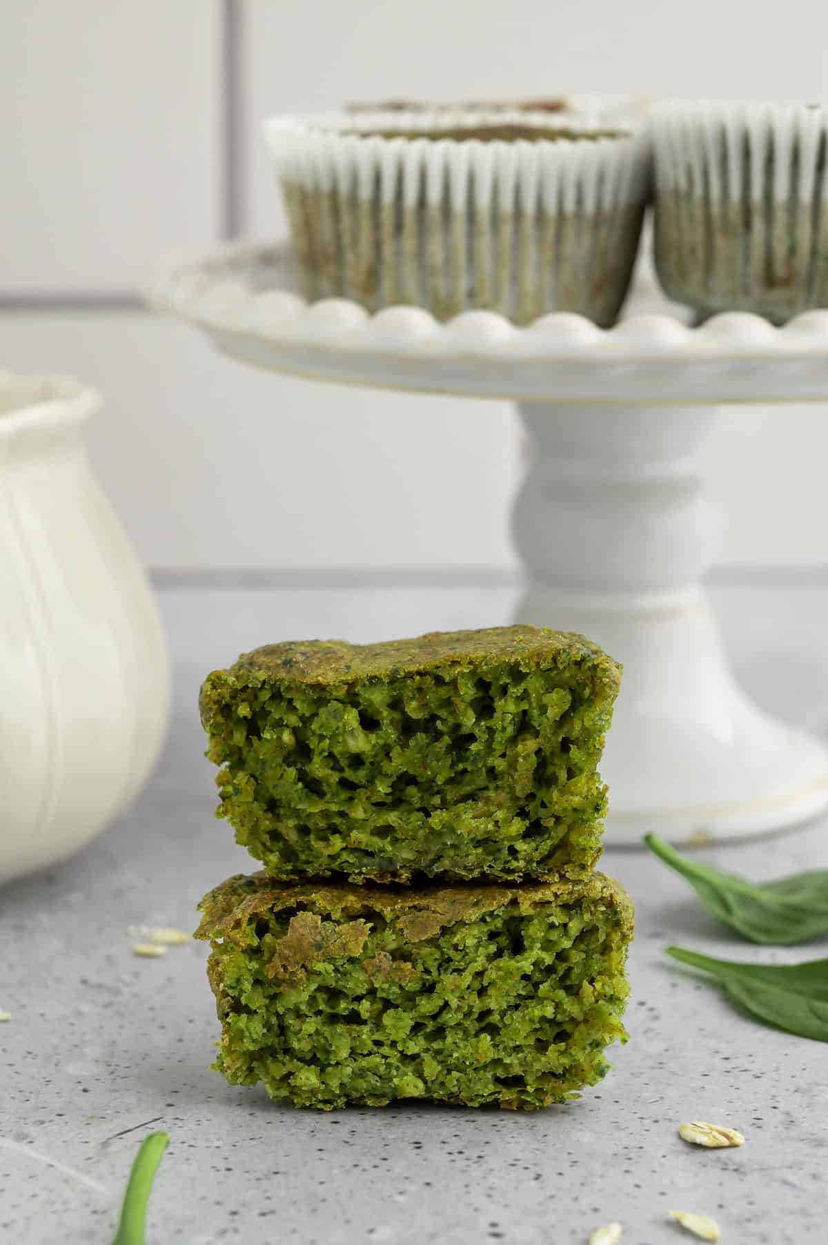 Two spinach banana muffins cut in half and stacked on a countertop.