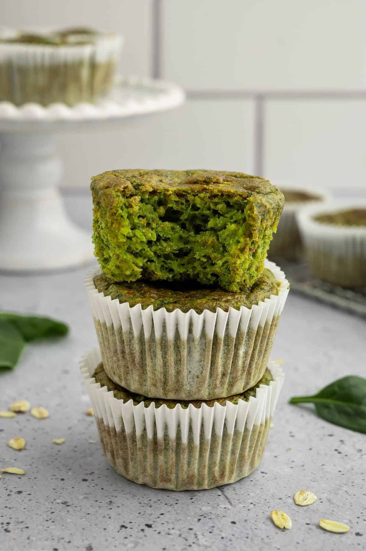Three spinach banana muffins stacked on a countertop.