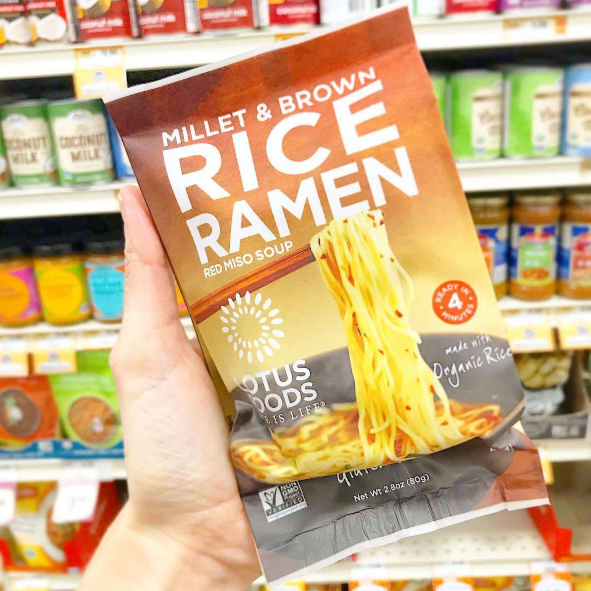 A hand holding a package of Lotus Foods Millet and Brown Rice Ramen.