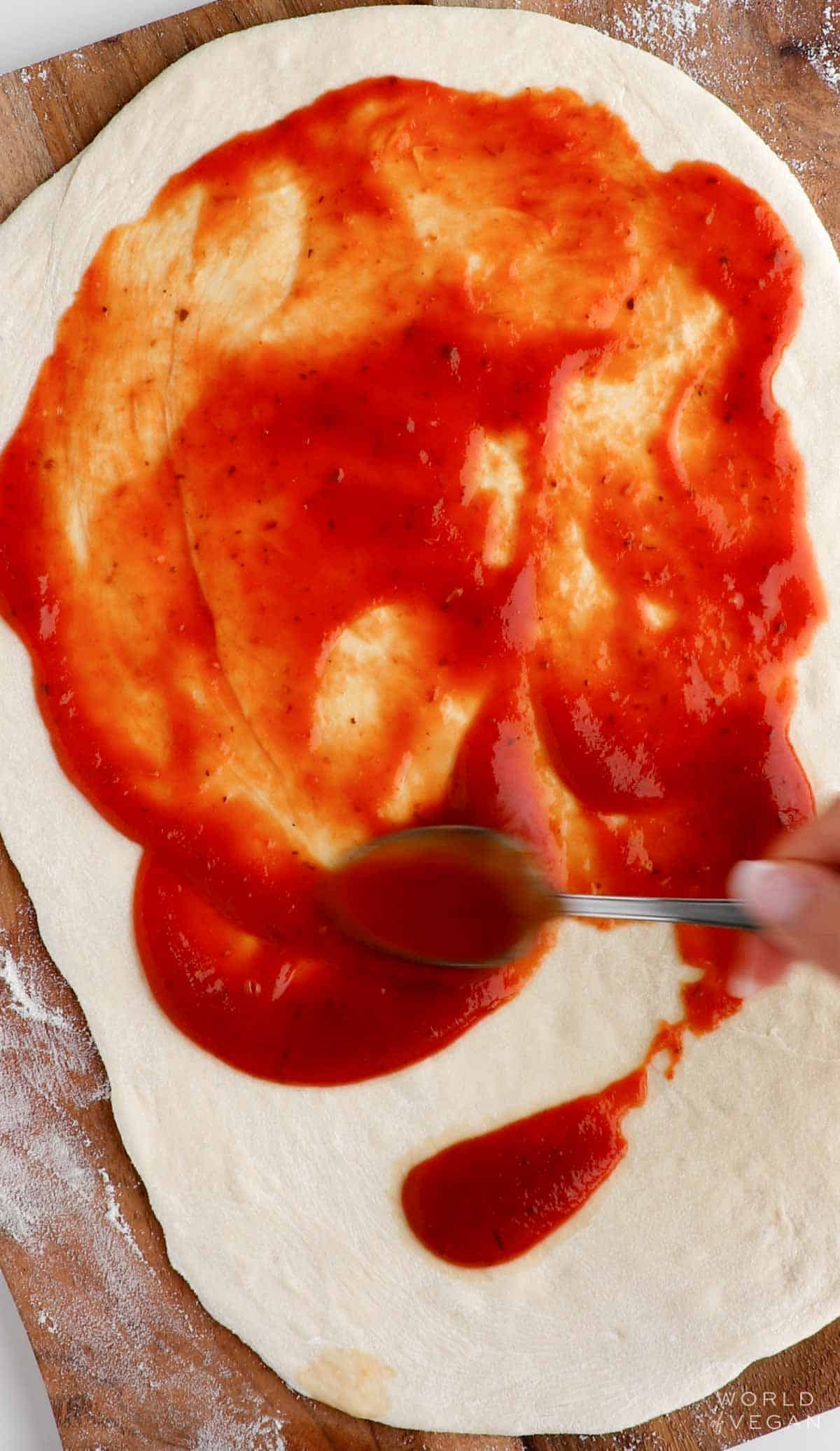 Spreading pizza sauce on rolled dough with a spoon.