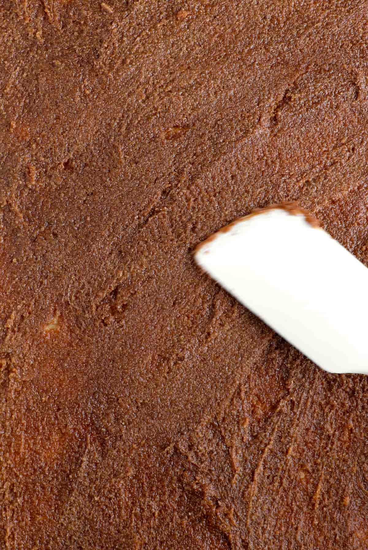 A silicone spatula spreading the filling on the cinnamon roll dough that's been rolled out.