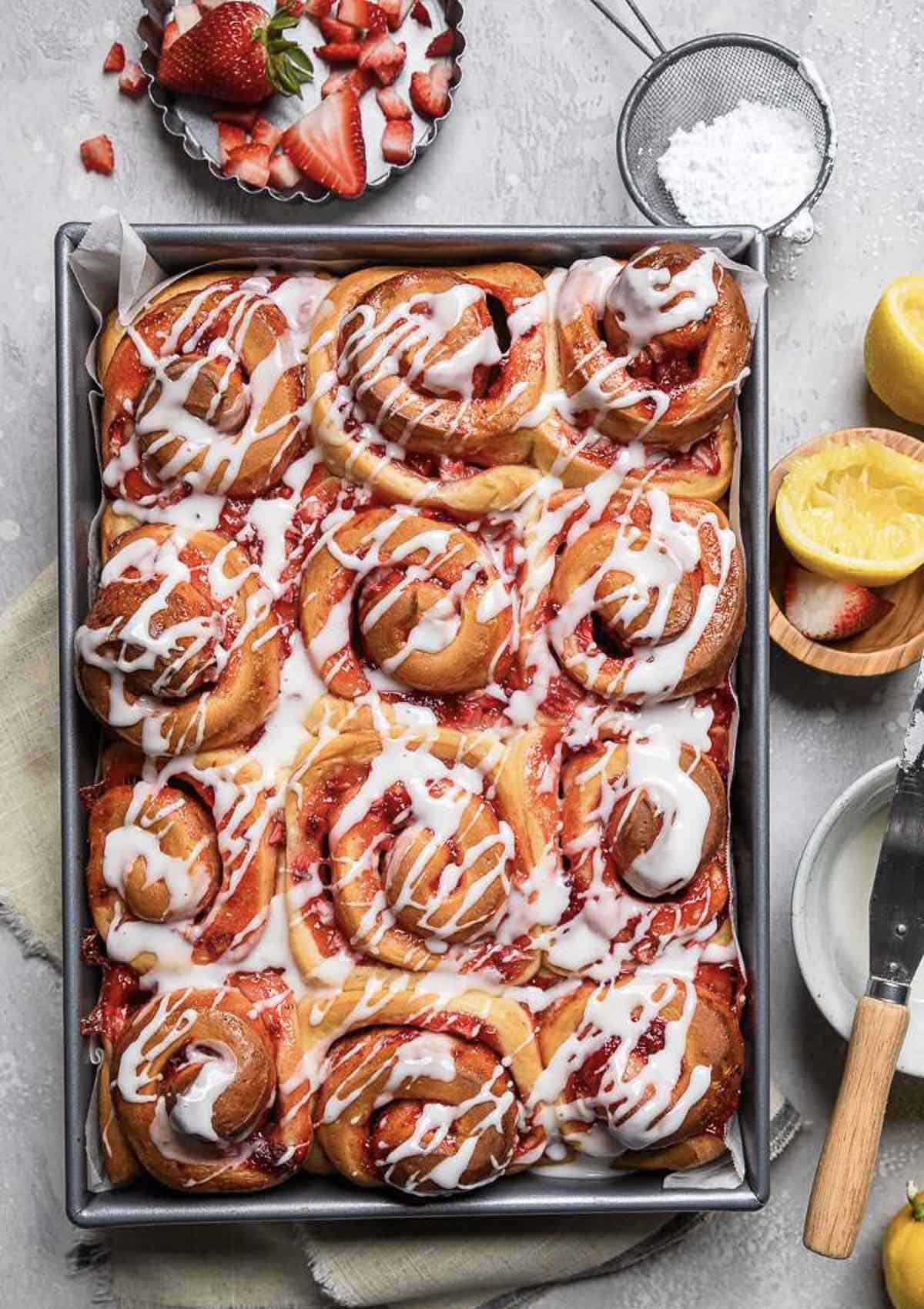 Baking pan of twelve strawberry flavored cinnamon rolls. 